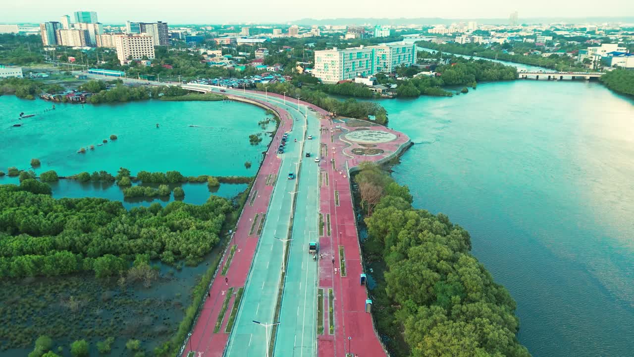 Drone footage of a riverside road lined with mangroves leading into a Philippine city skyline. Perfect for travel, urban planning, infrastructure, and lifestyle projects