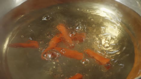 close up of carrot dropped into the boiling soup pot. vegetarian concept. sukiyaki or shabu