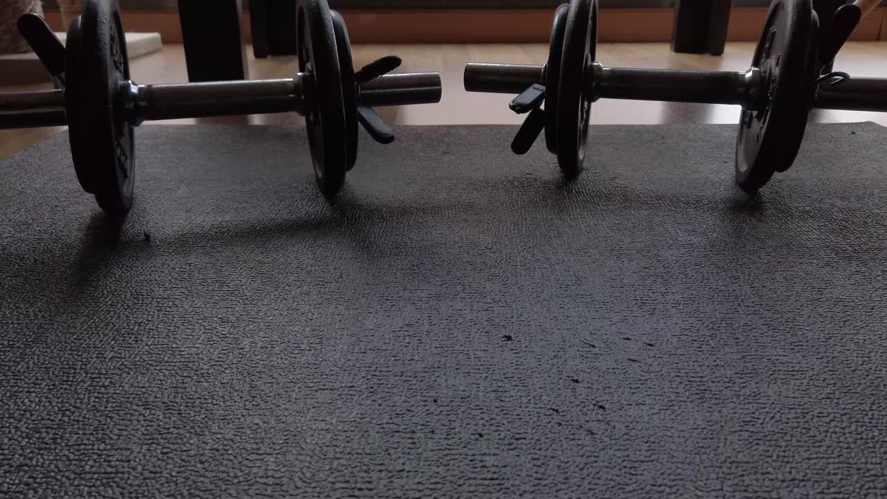 A dolly shot moving backwards focused in two dumbbells standing on a black mat