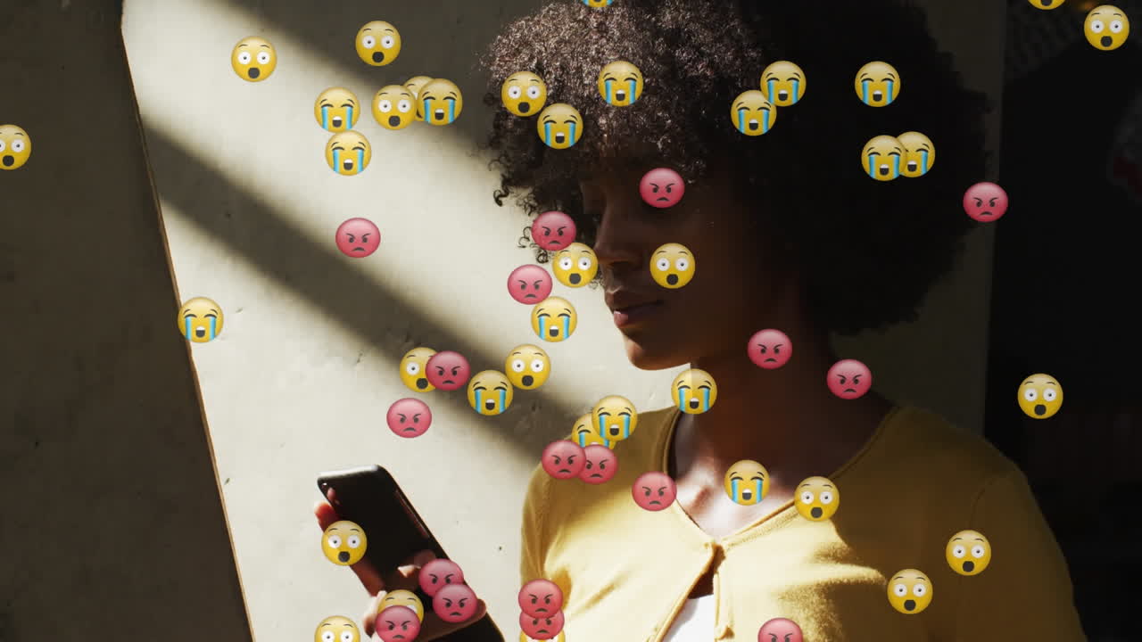 Animasjon av emojikoner fra sosiale medier over en afroamerikansk kvinne som bruker smarttelefon