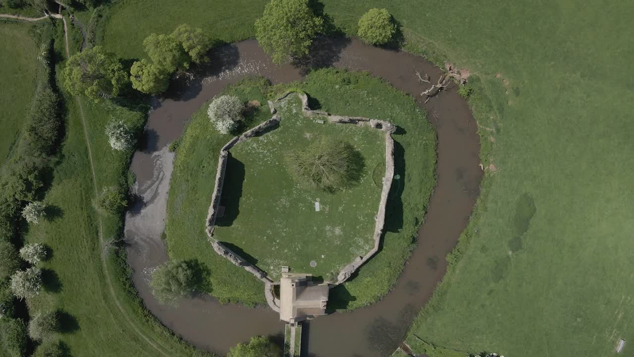 Aerial view of Stogursey Castle, a medieval castle in Somerset, England. Most of the site is in ruins, with a thatched gatehouse used for holiday's. Drone raising over the ruins and moat. 4K 60fps