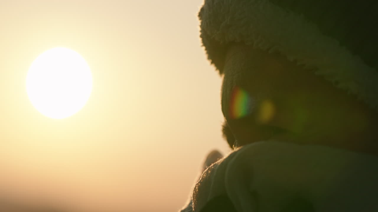 Cold woman with beanie and face covering at sunrise, close up handheld shaky sunflare in 4k