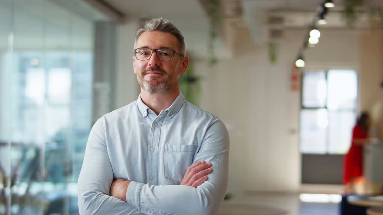 Portrait Of Smiling Mature Businessman Wearing Glasses  Standing In Modern Open Plan Office