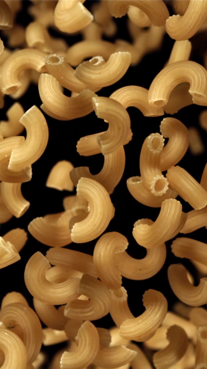 Pasta maccheroni secca che cade al rallentatore su sfondo nero.