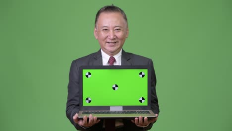 成熟した日本人のビジネスマンがラップトップを展示している