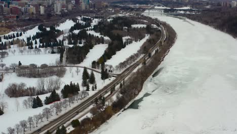 Flug-Aus-Der-Vogelperspektive-Fliegen-Sie-An-Einem-Düsteren-Winternachmittag-über-Den-Victoria-Park-Am-Schneebedeckten,-Eisigen-North-Saskatchewan-River,-Umgeben-Von-Ruhigen-Golfplätzen,-Die-Die-Beiden-Innenstadtbereiche-5-7-Trennen