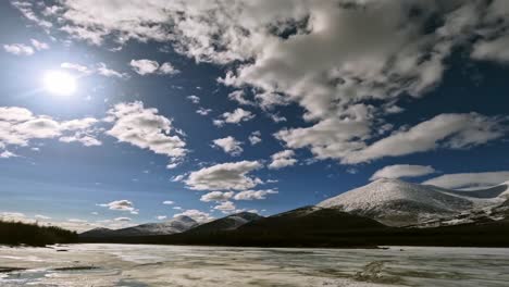 timelapse of a frozen river against the backdrop of mountains and floating sunny clouds