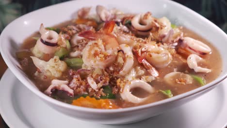 authentic thai soup with delicious spices and seafood in a white bowl spinning close up