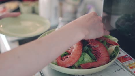 hands of a woman putting prawns on top of the vegetable salad. - close up shot
