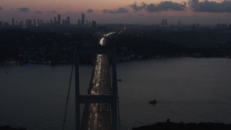 Istanbul-15-July-Martyrs-Bosphorus-Bridge-at-Dusk-or-Night-with-City-Skyline-Silhouette-and-Car-traffic-flowing-out-of-the-City-lights,-Aerial-slide-right