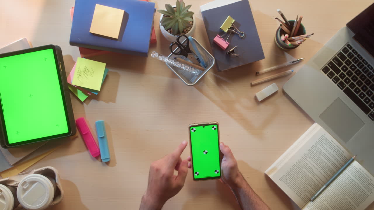 Manos tocando smartphone y tableta con pantalla verde en escritorio de oficina