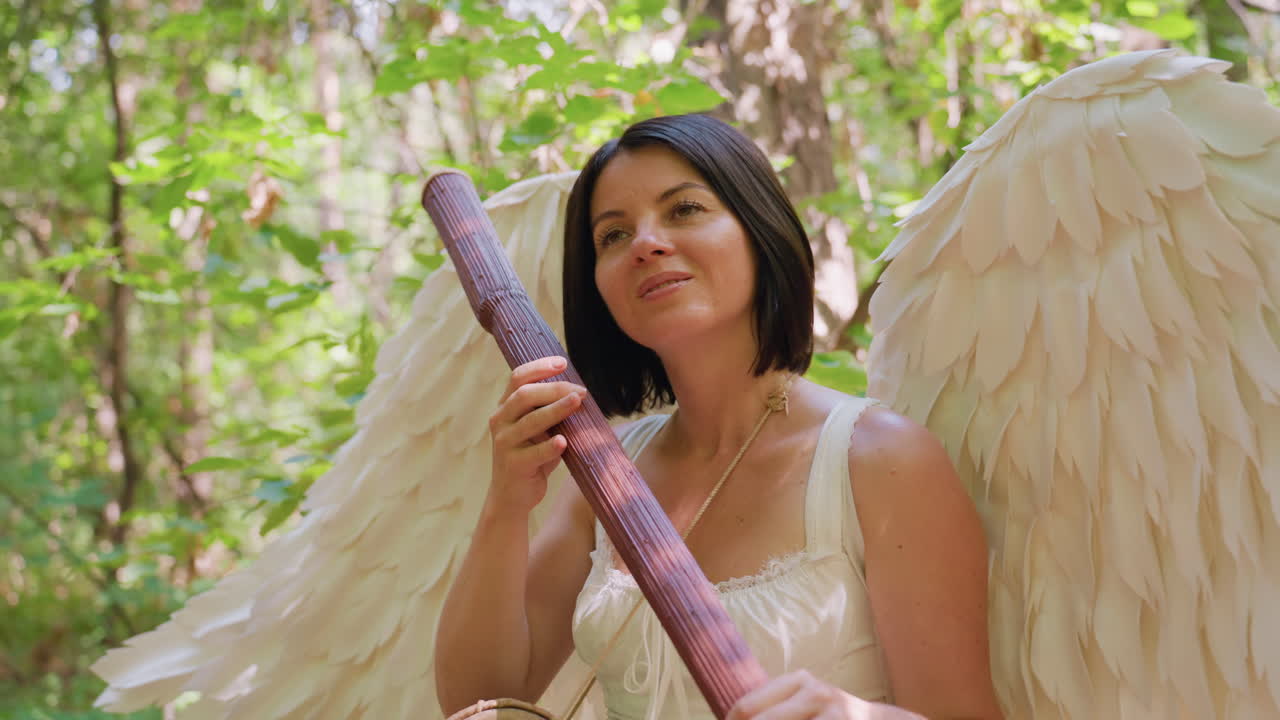 Nature lover seated in forest holding wooden staff, tapping it gently like harp with drum hanging around neck, surrounded by green sunlight and soft leaves, expressing harmony