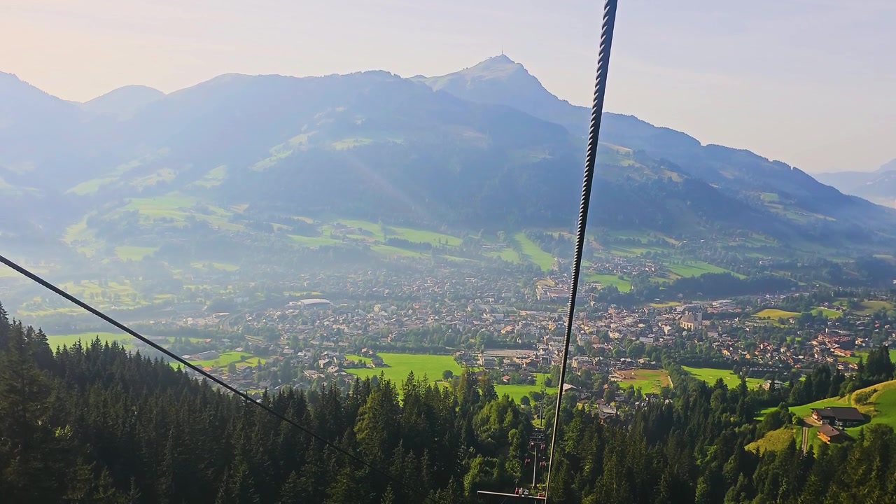 Giro in funivia alpina sopra una valle verde, con tetti di villaggi, linee di impianti di risalita, foresta di conifere e paesaggi turistici montani soleggiati in una tranquilla regione turistica europea.