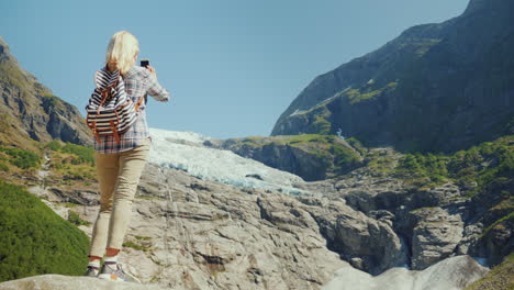 an active traveler woman stands on a rock photographs a beautiful glacier in norway journey through