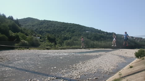 people walking across a suspension bridge over a river in mountains