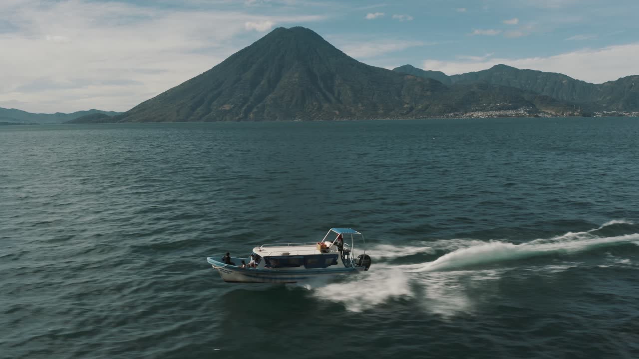 vuelo aéreo de drones junto a un bote a motor que viaja en el lago atitlán, guatemala con hermoso volcán y paisaje de agua azul