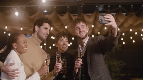 group of four happy multiethnic friends taking a selfie video and toasting with champagne glasses at new year's eve party