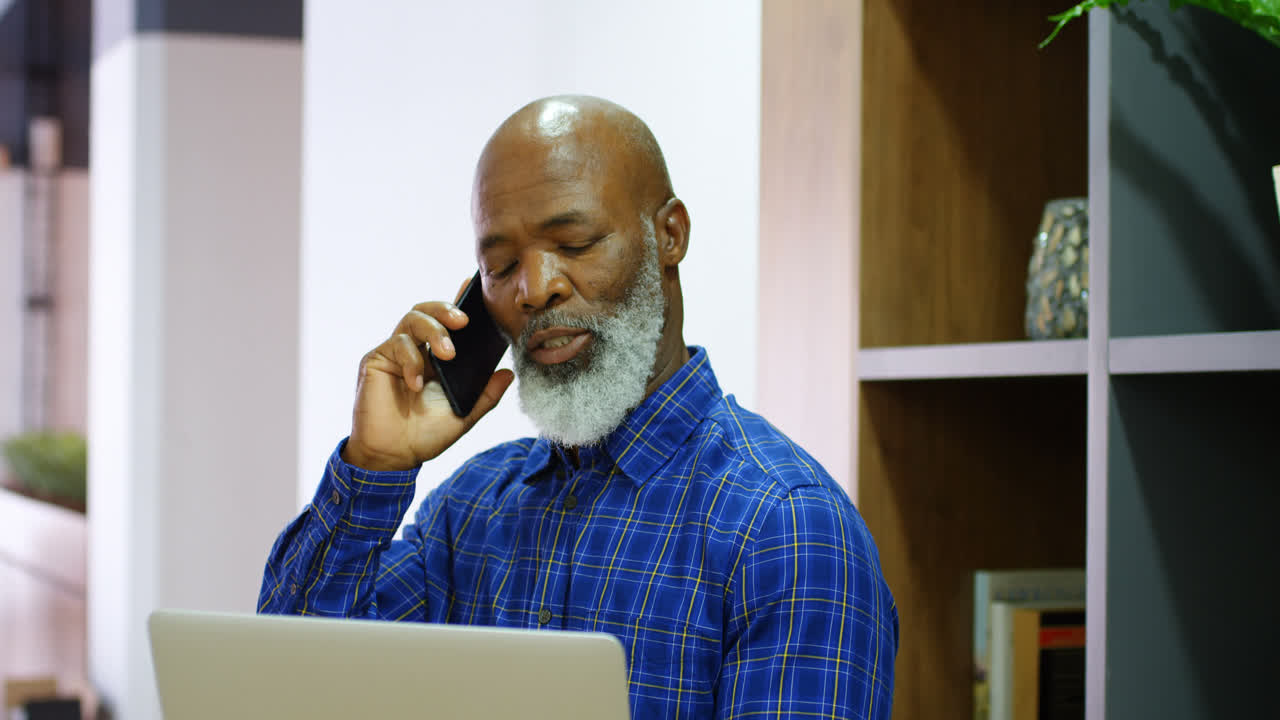 Senior man talking on mobile phone while using laptop 4k