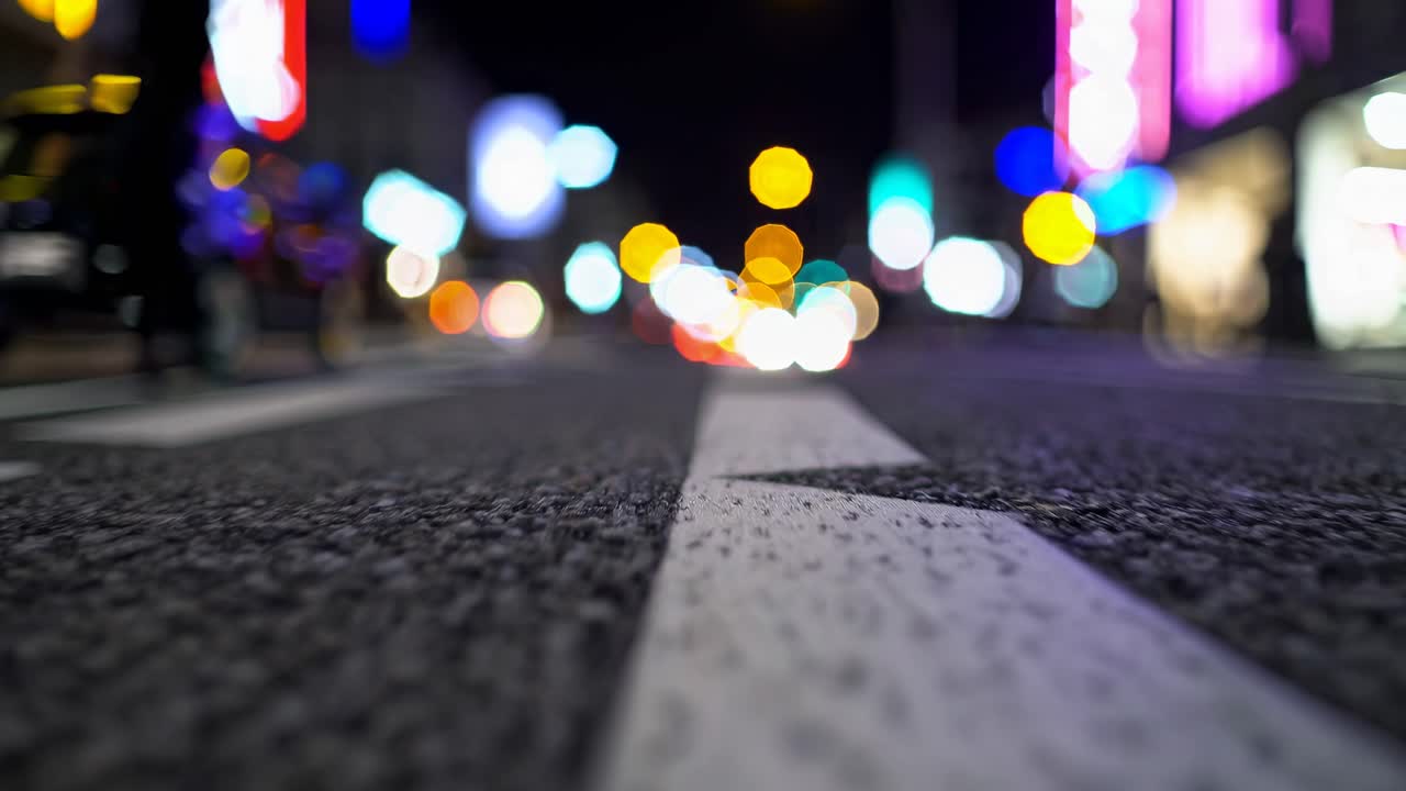 Ripresa video dal basso di una strada cittadina di notte, che mostra luci bokeh colorate e una strada a fuoco