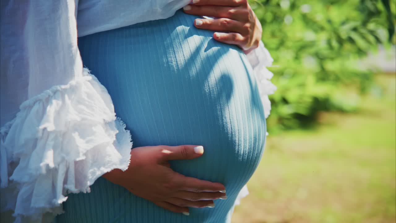 Pregnant Woman Gently Caressing Her Belly Outdoors