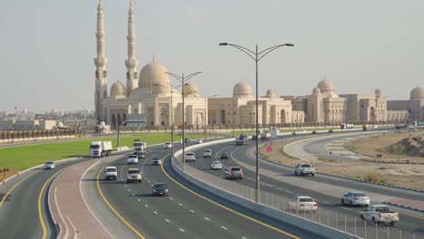 vehículos que pasan por la autopista de la ciudad moderna con la mezquita de la universidad al qasimia en el fondo en sharjah, emiratos árabes unidos