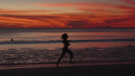 silhouette of a woman jogging along flamingo beach, costa rica, under a dramatic sunset sky with orange and red tones.