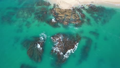 aerial view looking down at rocky coastline with waves crashing and tropical blue water