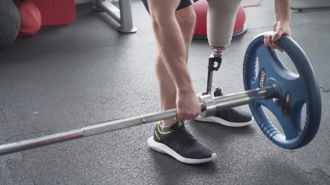 Disabled man with prosthetic leg puts weights for excercise at the gym