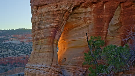 a drone glides slowly toward a majestic red rock arch, capturing the golden sunrise light streaming through.