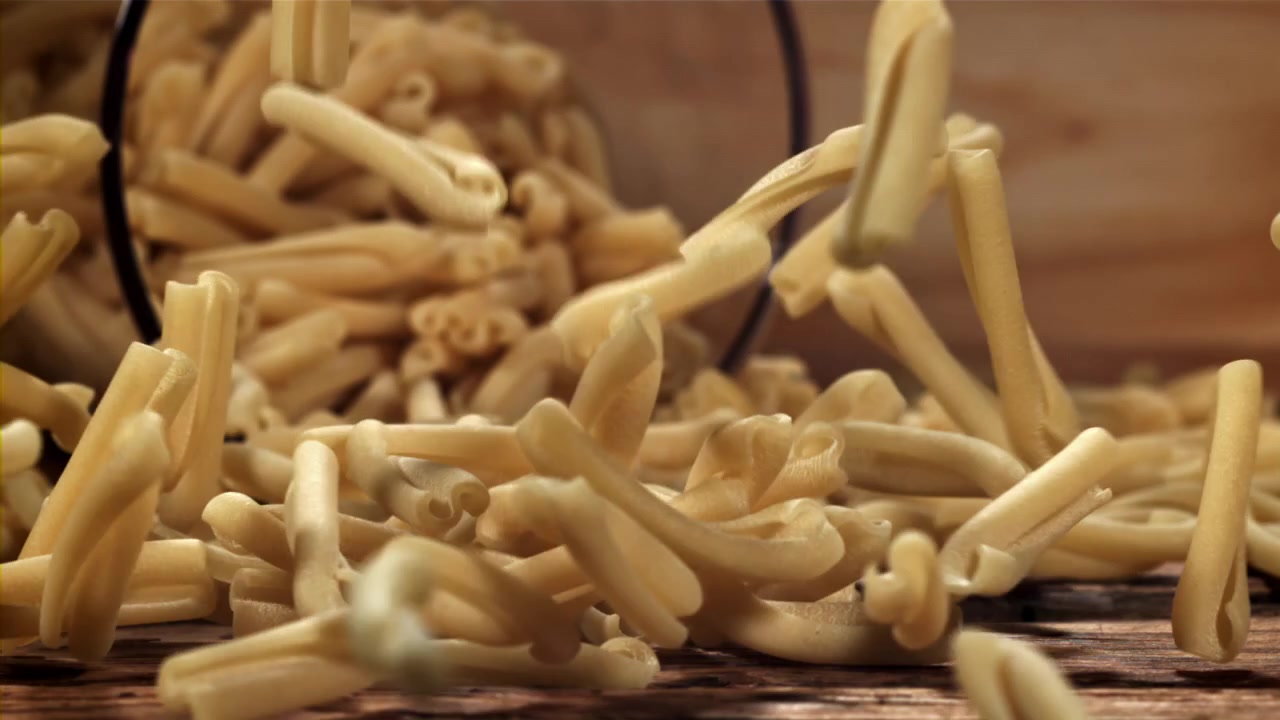Al rallentatore: pasta italiana secca che cade su un tavolo di legno rustico.