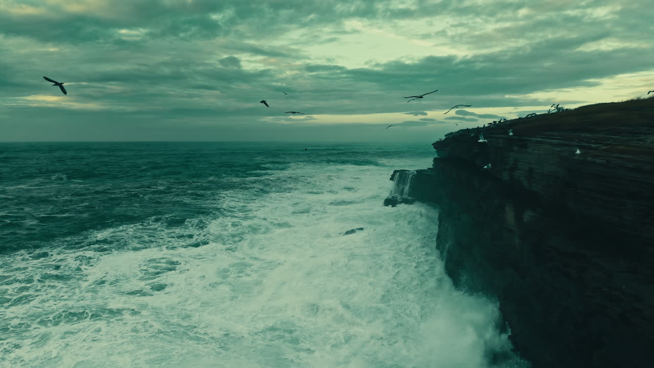 Dramatic Ocean Waves Crashing Against Rocky Cliff with Flying Seagulls