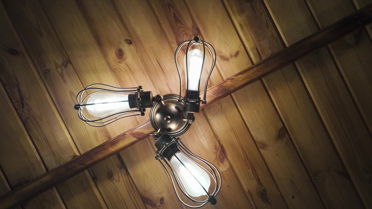 Vista statica di un lampadario vintage da soffitto con quattro lampadine a vista, montato su un soffitto a doghe di legno in un ambiente rustico
