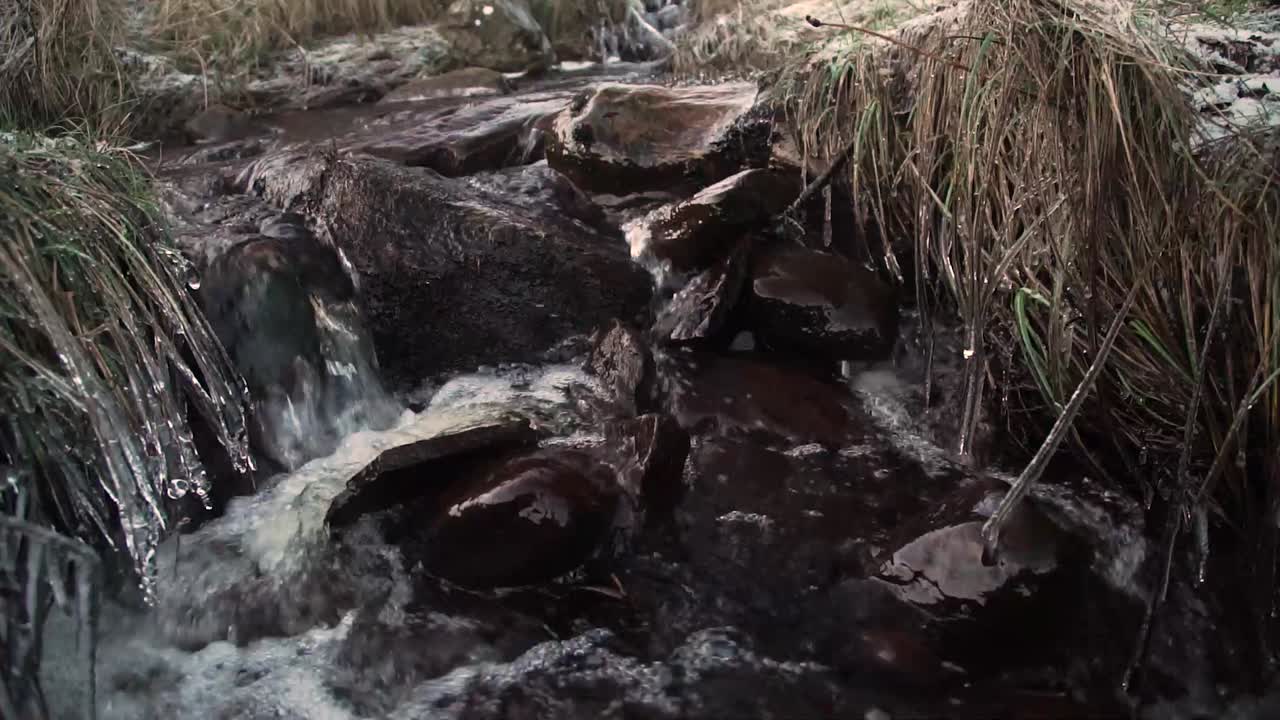 Freezing river stream flowing quickly between still black rocks winter morning
