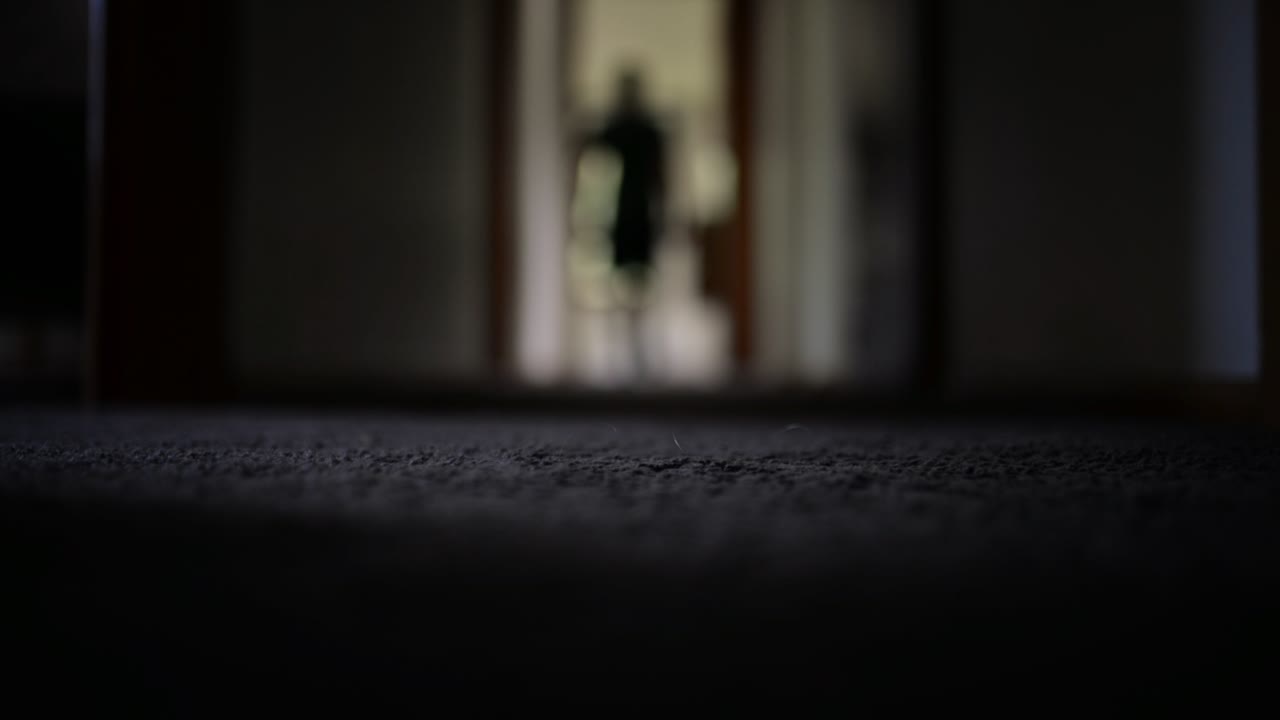 Personne marchant dans un couloir sombre moquetté à la maison.