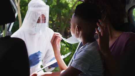 african american mother and son sitting in car having covid test done by medical worker outdoors