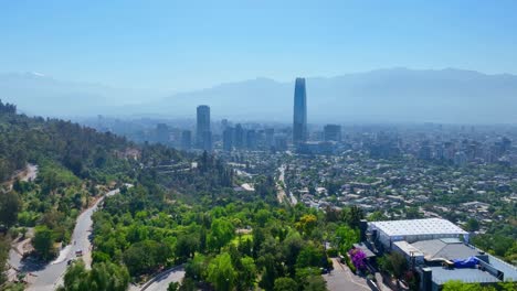 forward drone shot from san cristóbal hill overlooking santiago’s financial district with costanera tower and andes mountains in the background