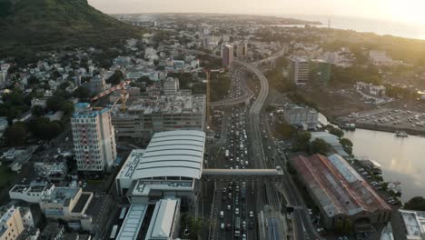 Toma-Aérea-Inclinada-Hacia-Arriba-Del-Tráfico-En-La-Autopista-En-Port-Louis-Durante-La-Puesta-De-Sol-En-Mauricio