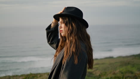 model posing holding hat at ocean coast gloomy evening close up. serious woman