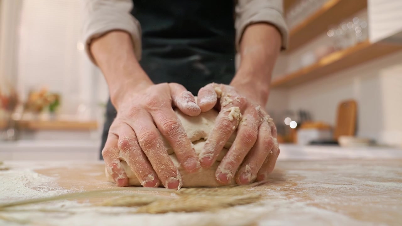Primer plano de las manos de un chef amasando masa en una mesa de madera.