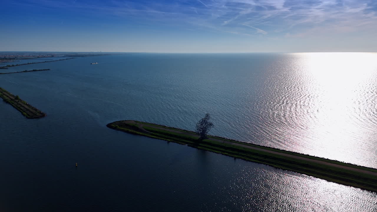 Approaching the iron sculpture of the man figure sitting on the dike. Modern art piece on the Markemeer lake in Lelystad, The Netherlands. Aerial view.