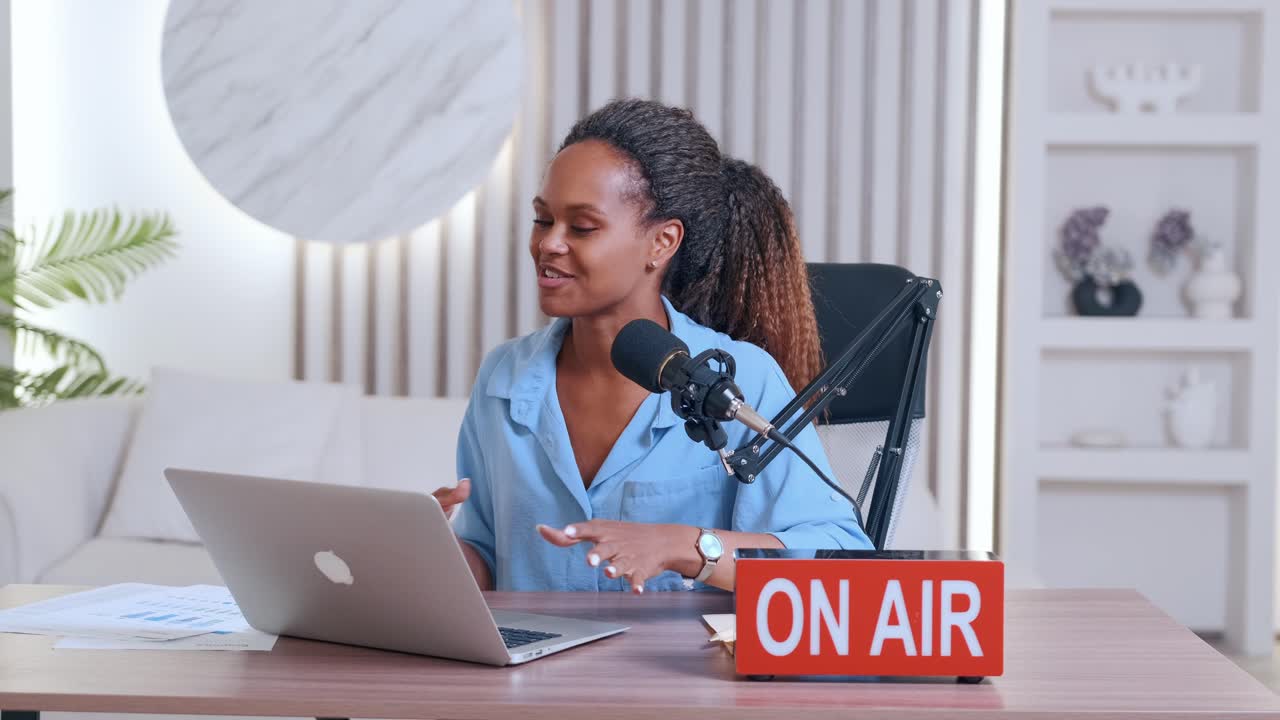 una joven bloguera afroamericana presenta un podcast sentada en la mesa con una computadora portátil