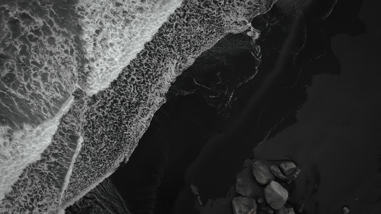 кинематографический сверху вниз черный песчаный пляж воздушный, волны разбиваются на вулканическом песке исландии, летая вверх