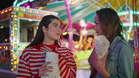 best friends talking gossiping at luna park. smiling teenagers eating snacks