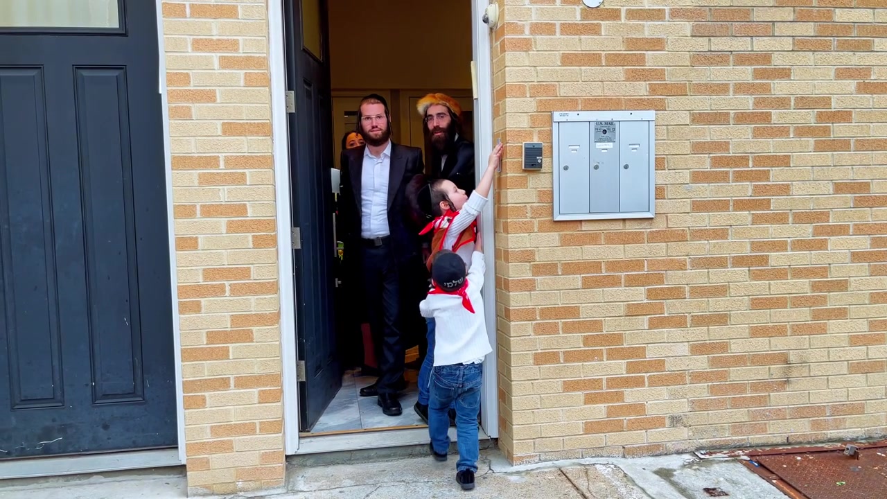 New York, USA, 9 marzo 2022: Gruppo ebraico ortodosso all'ingresso di un appartamento a Brooklyn. Adulti e bambini stanno all'ingresso di un appartamento a Brooklyn accanto a cassette della posta e una facciata in mattoni, con luce diurna.