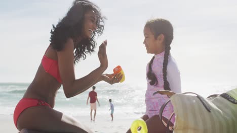 madre hispana feliz aplicando crema solar en la cara de su hija en la playa