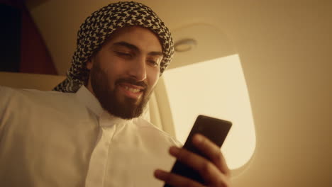 Successful man surfing web at airplane window closeup. Arabian hold smartphone