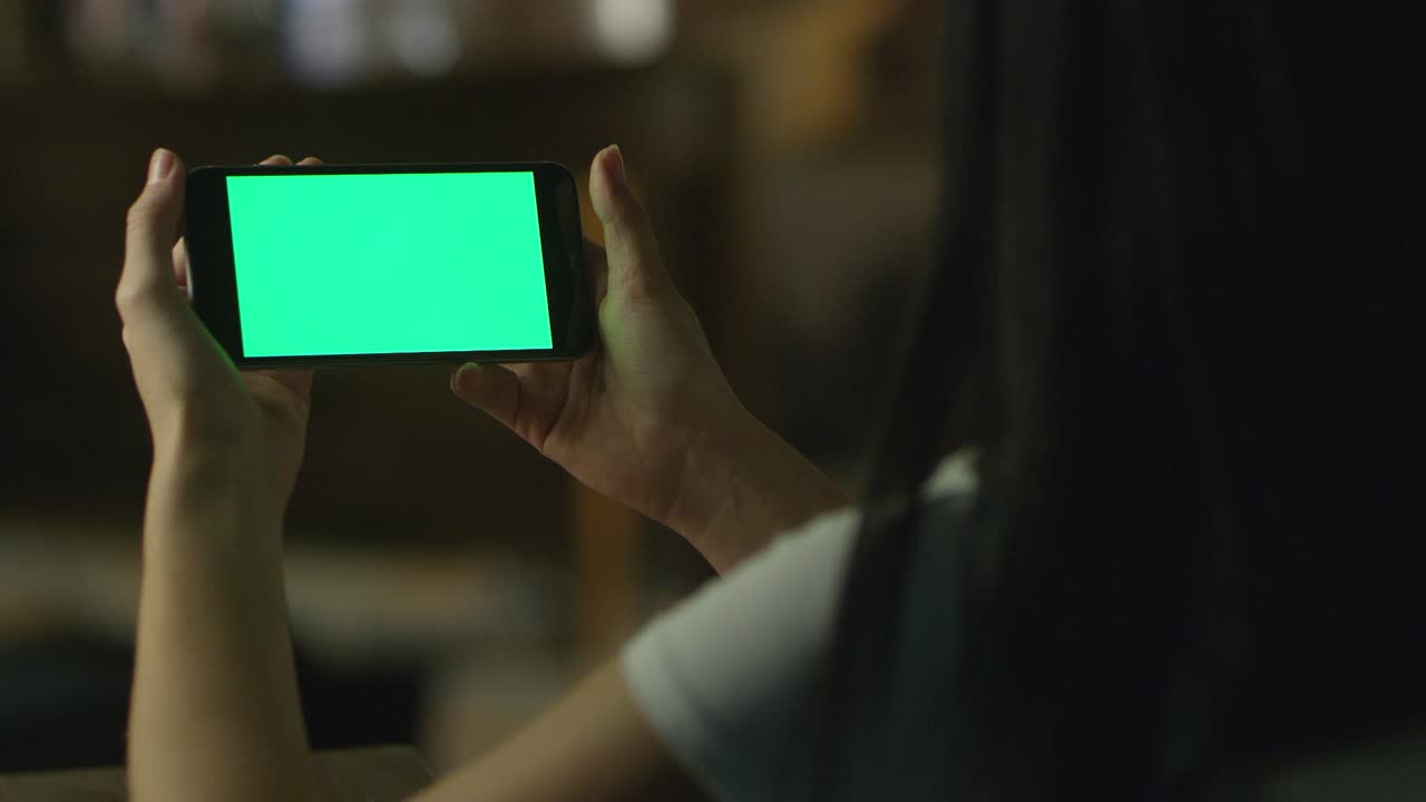 una adolescente está usando un teléfono inteligente con pantalla verde en modo paisaje por la noche. estilo de vida casual.