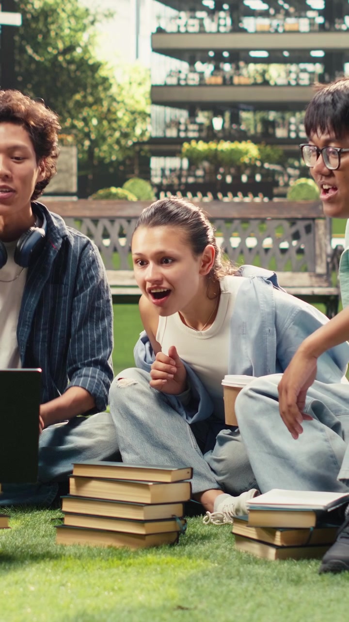 Vertical Video Diverse students checking notes on laptop with stack of books