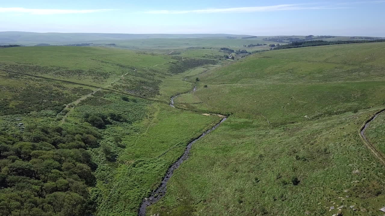 amplia toma aérea que sigue hacia adelante y hacia abajo, con wistmans wood, un río y un páramo cubierto de hierba configurando la escena