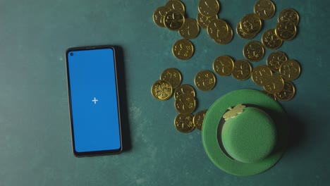 overhead studio shot of green leprechaun top hat with gold coins and blue screen mobile phone to celebrate st patricks day 3